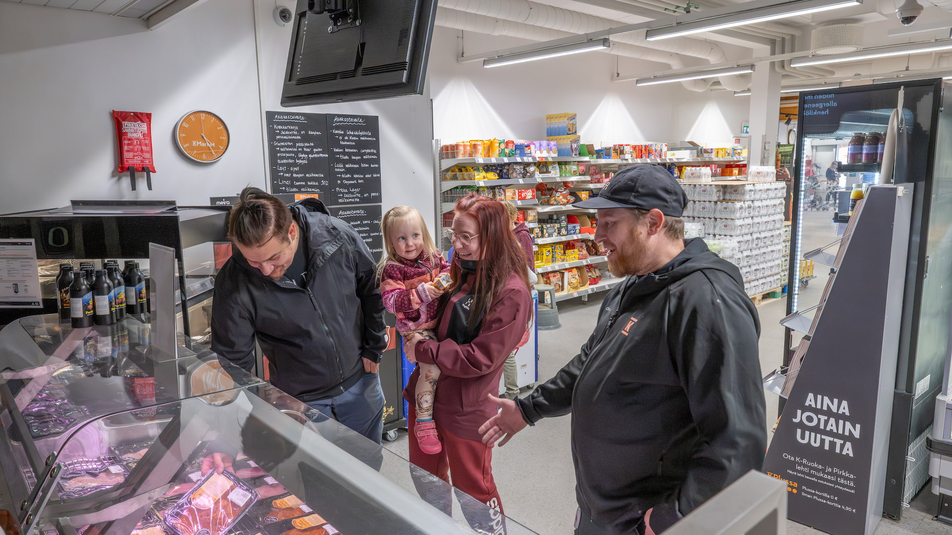 Myyjä esittelee tuotteita kaupassa naiselle, miehelle ja pienelle lapselle.